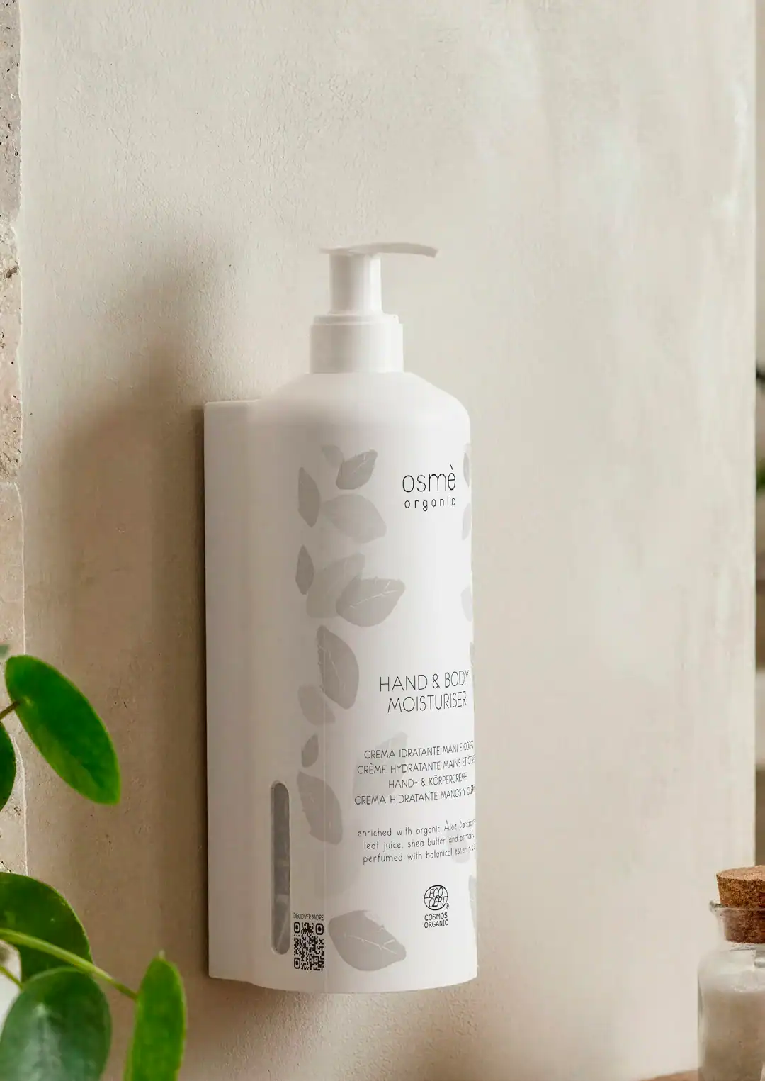 Dispenser Osmè Organic su una parete chiara con dettagli botanici